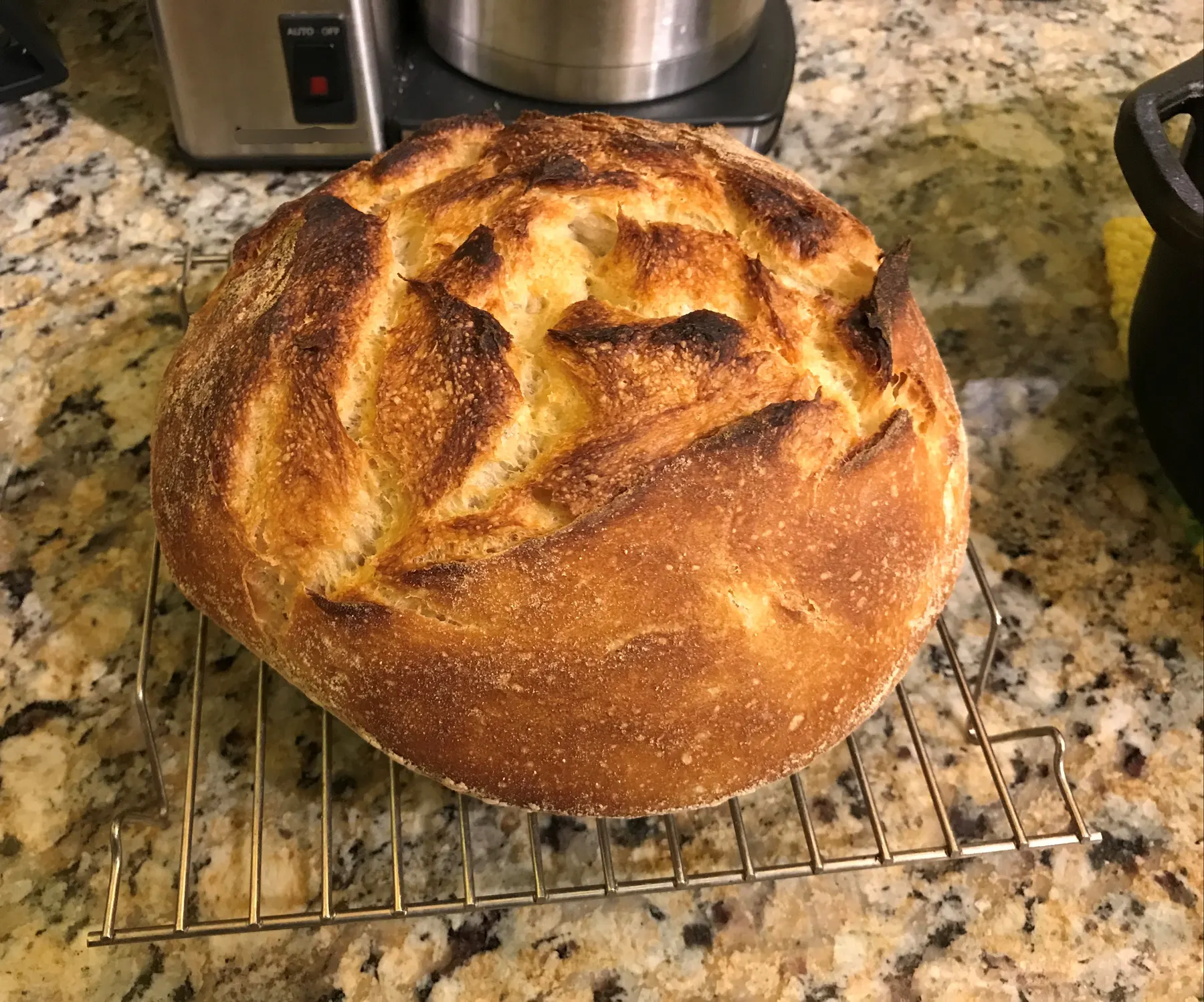 A round sourdough loaf with a dark scored crust cooling on a wire rack