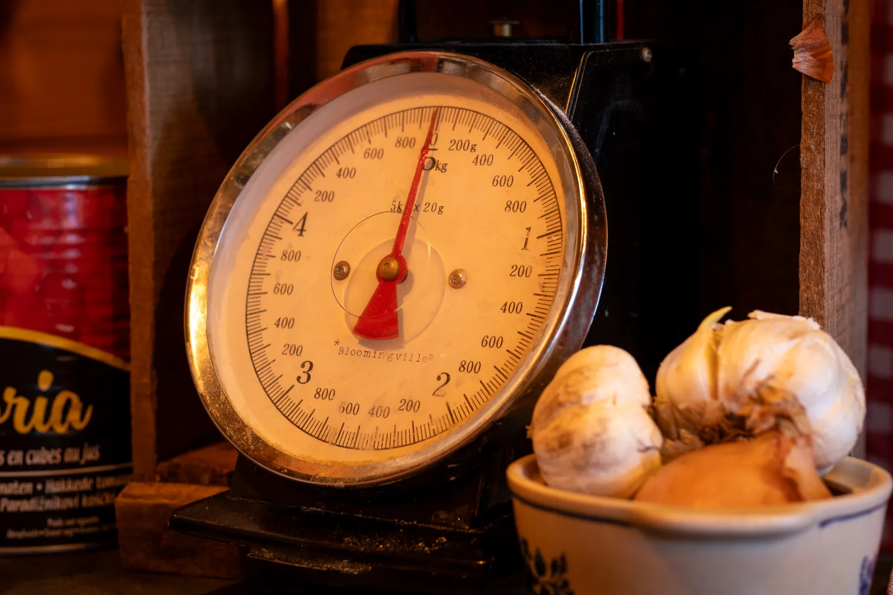 An old brass kitchen scale beside a bowl of onions in warm lamplight
